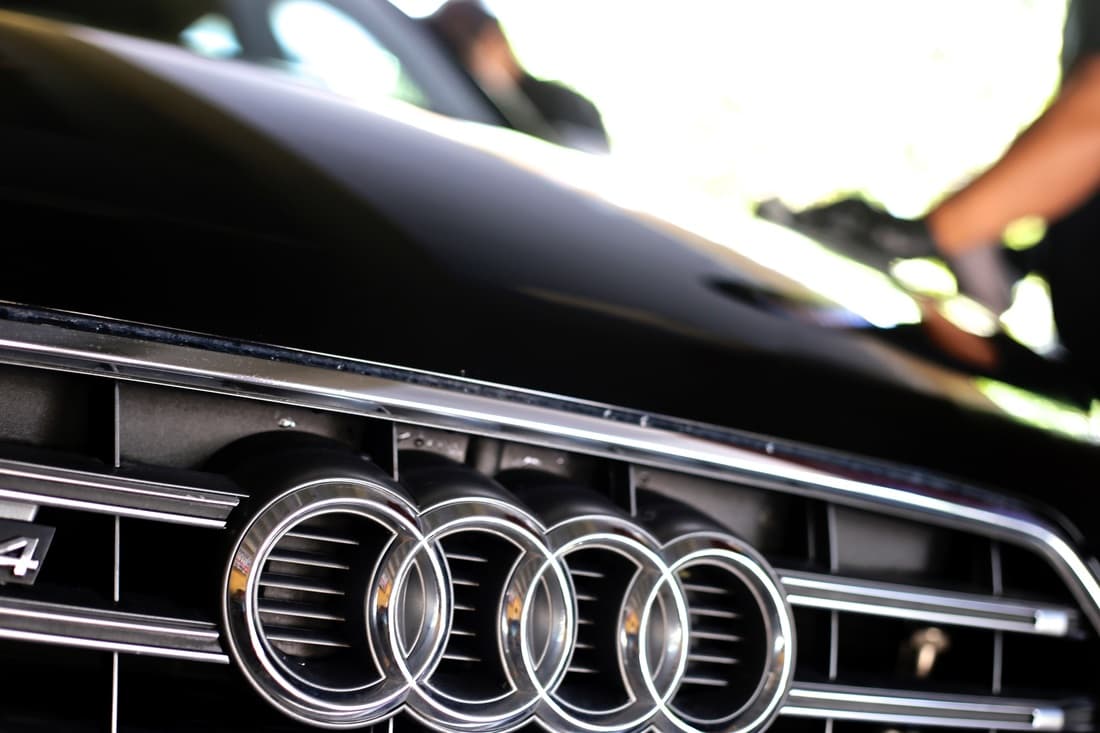 A detailer hand-finishing the hood of a black Audi